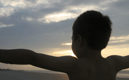 Boy opening arms wide to beach sunrise