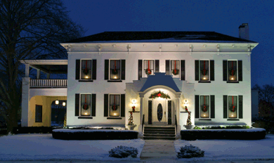 House in snow, lit with lamps and hung with Christmas wreaths